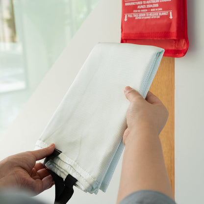 Person holding a white fire blanket with a red fire extinguisher in the background