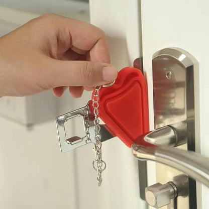 Red heart-shaped portable hotel door lock attached to a door handle with keys hanging from it.