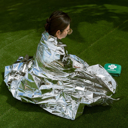 A female sitting on the green grass wrapped in an emergency blanket included with snake bite first aid kit